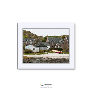 A white-framed photograph of a coastal village with houses, boats, and a rocky shoreline.