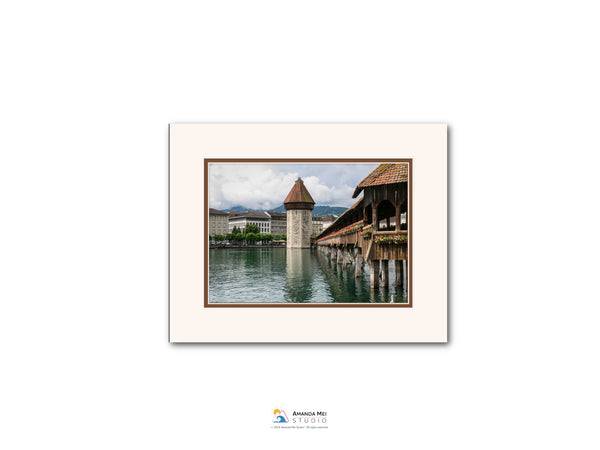 a picturesque scene of a wooden bridge with a tower on the water, surrounded by lush greenery and a cloudy sky.