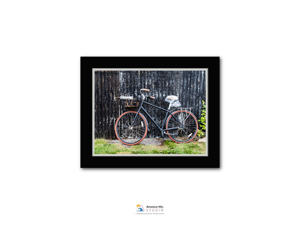 A black bicycle with red accents is leaning against a wooden fence.
