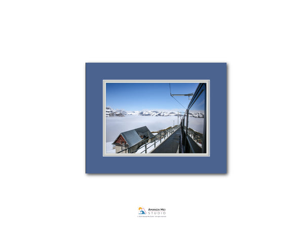 A framed photograph of a snowy mountain landscape with a ski lift and a building in the distance.