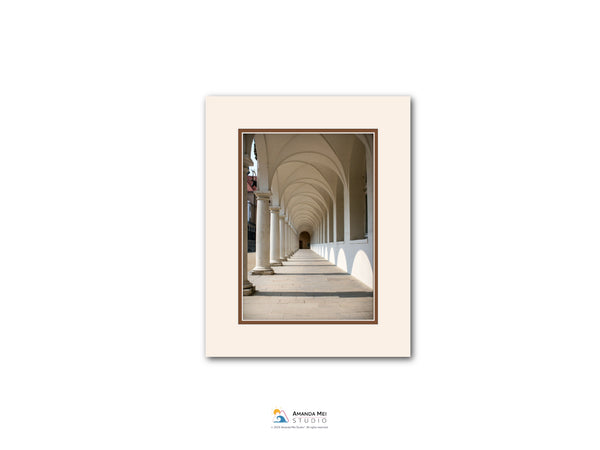 a long, arched hallway with white columns lining the sides, creating a sense of depth and perspective.