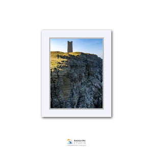 a tall tower perched atop a rocky cliff, with a clear blue sky in the background.