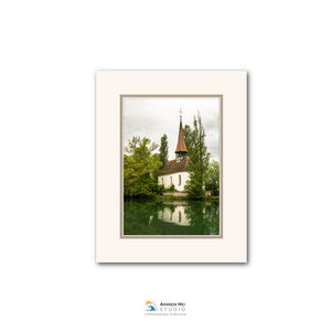 A white frame containing a photograph of a church with a steeple and a lake in the background.
