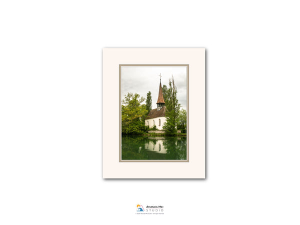 A white frame containing a photograph of a church with a steeple and a lake in the background.