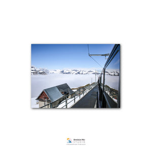 A snowy mountain landscape with a ski lift and a building in the foreground, all under a clear blue sky.
