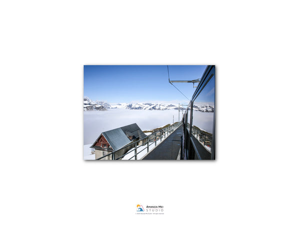 A snowy mountain landscape with a ski lift and a building in the foreground, all under a clear blue sky.