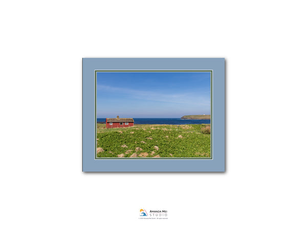 A red house sits on a grassy field, with a body of water visible in the distance.