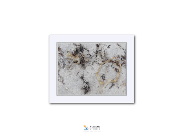 The image is a photograph of a sandy beach with various textures and patterns, including small rocks and shells.