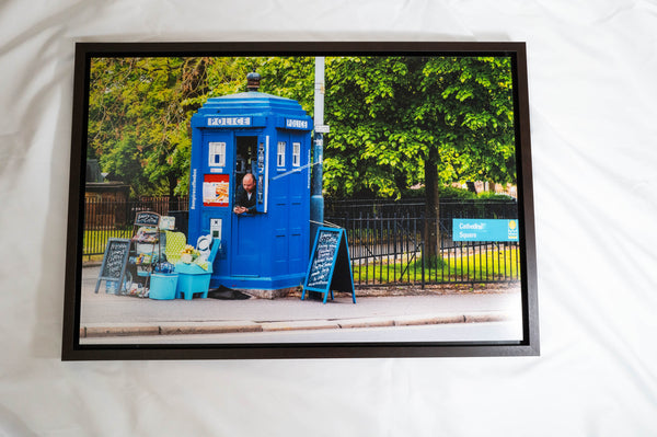 A blue police box with a sign that reads "Police" is situated on a street, with a person standing inside the box.