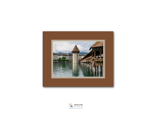 a picturesque scene of a wooden bridge with a tower, situated over a body of water. The bridge is surrounded by lush greenery, creating a serene and tranquil atmosphere. The image is framed within a brown border, and the text "AQUA MOS Studio" is visible, indicating the source or creator of the image.