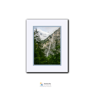 A framed photograph of a mountainous landscape with a waterfall, surrounded by pine trees.