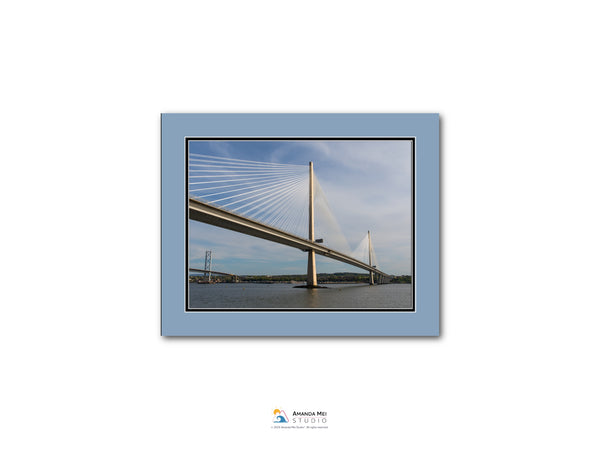 A large suspension bridge spanning a body of water, with its cables and towers visible against a blue sky.