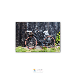 A black bicycle with red wheels is leaning against a black corrugated metal fence.