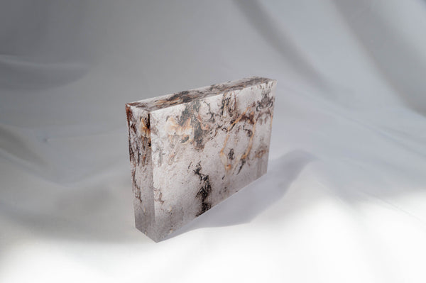 A rectangular, textured object with a weathered appearance, possibly a piece of stone or concrete, is shown against a plain white background.