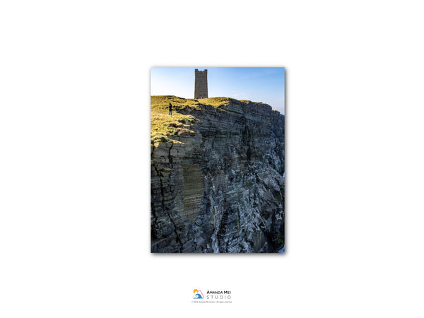 a tall tower perched atop a rocky cliff, with a clear blue sky in the background.