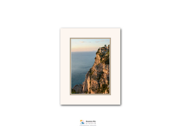 The image is a framed photograph of a cliff overlooking the ocean, with a sunset sky in the background.