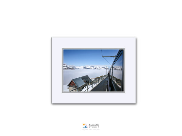 A snowy mountain landscape with a ski lift and a building in the distance, captured from a high vantage point.