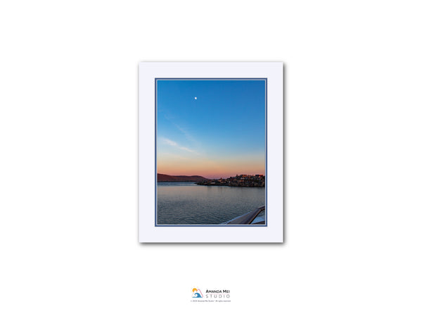 a serene sunset over a body of water, with a small town or village visible in the distance.