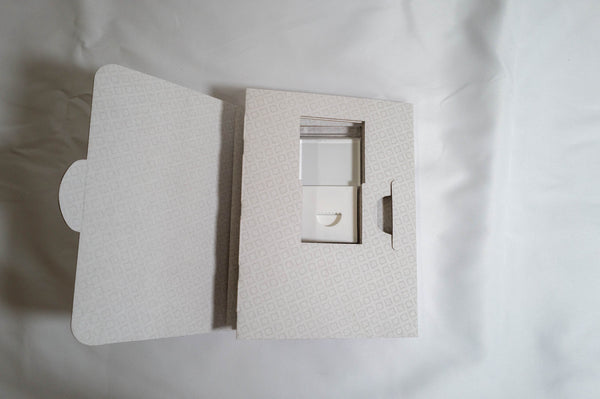 a white box with a cutout, possibly containing a small object or a compartment, placed on a white surface.