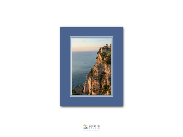 The image is a framed photograph of a cliff overlooking the ocean, with a sunset in the background.