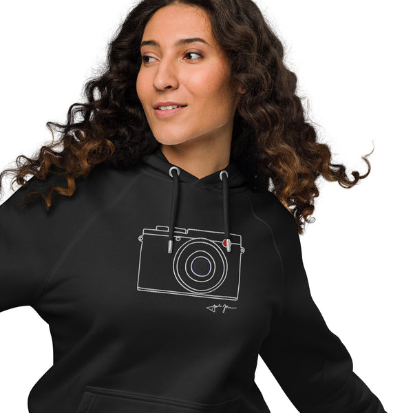 A woman with long curly hair wearing a black hoodie with a white graphic of a camera on it.